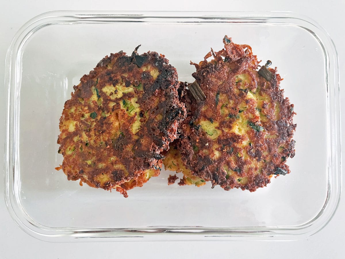 Leftover zucchini fritters are kept in a glass food storage container.