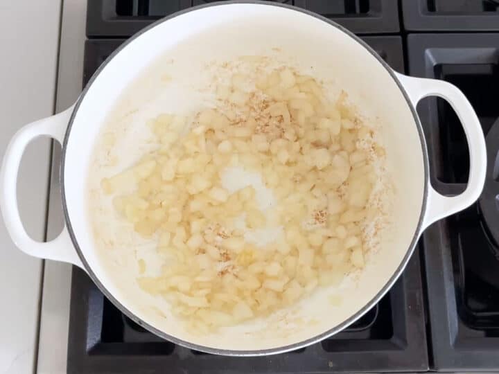 Onions are sauteed in a white stockpot.