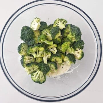 Adding the broccoli florets to the dressing in the bowl.