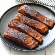 Four blackened salmon fillets are served on a black plate.