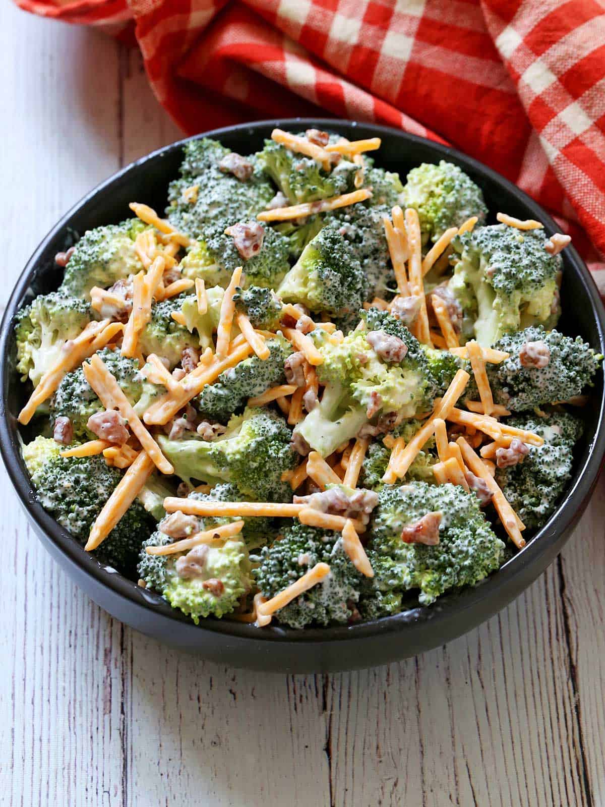 Broccoli salad is served in a black-colored bowl.