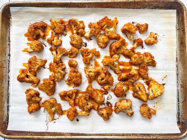 Buffalo cauliflower is ready on a parchment-lined baking sheet.