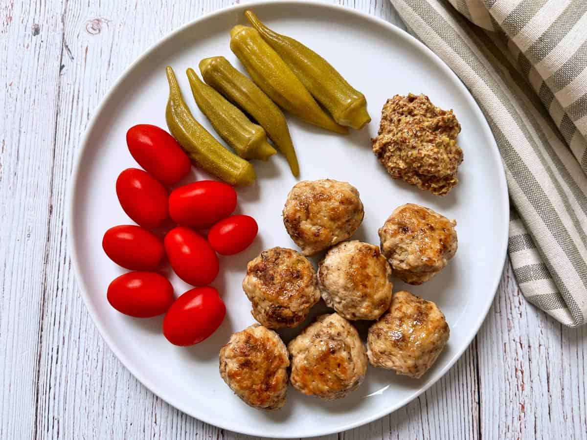 Leftover chicken meatballs are served with tomatoes, pickles, and mustard.