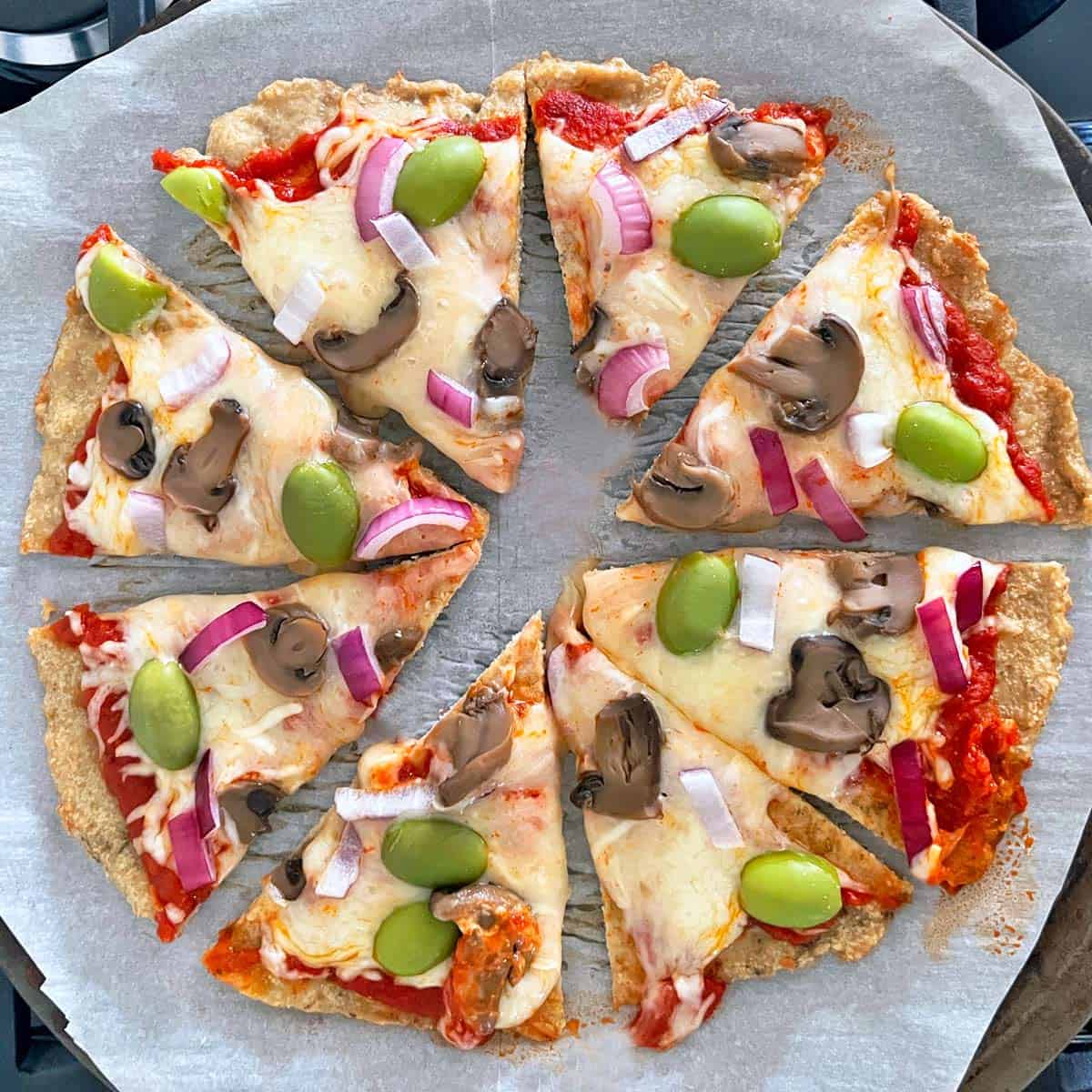 Chicken crust pizza is topped with red onions, mushrooms, and green olives.
