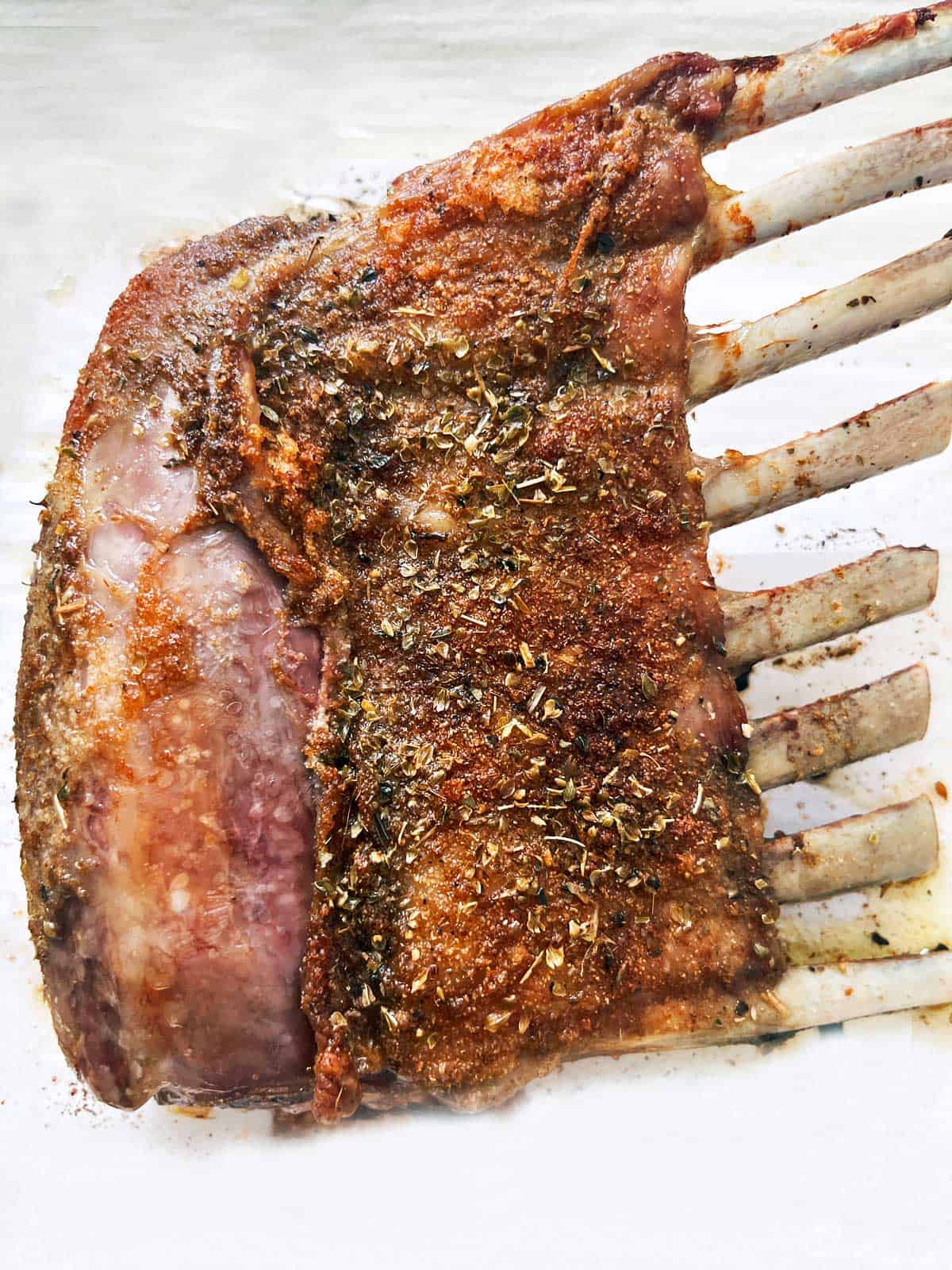 A roasted rack of lamb on a parchment-lined baking sheet.