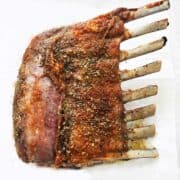 A roasted rack of lamb on a parchment-lined baking sheet.