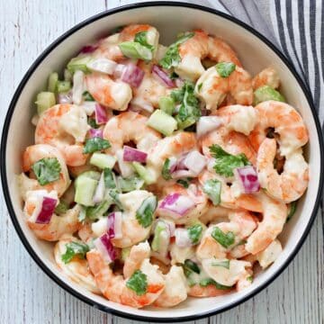 Shrimp salad with celery and red onions is served in a white bowl with a dark rim.