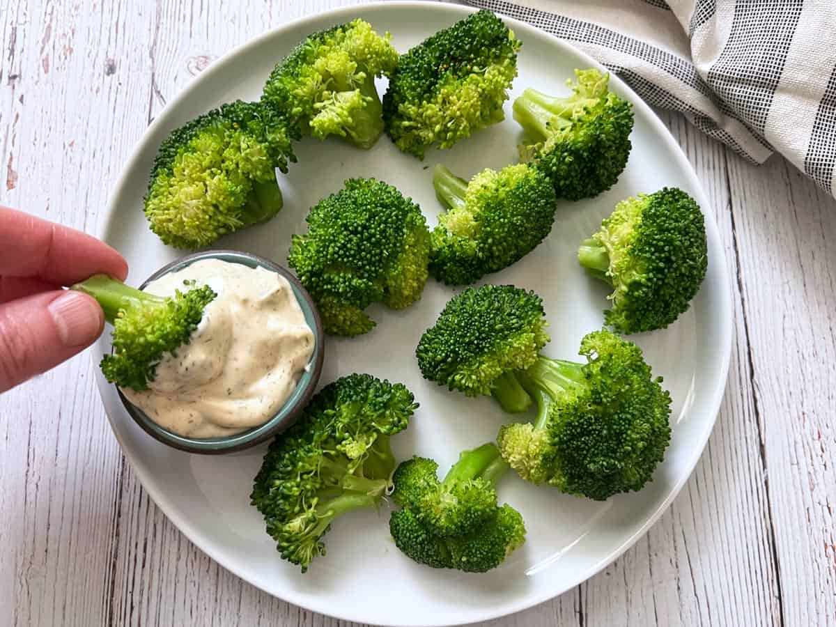 Steamed broccoli is dipped into tartar sauce.