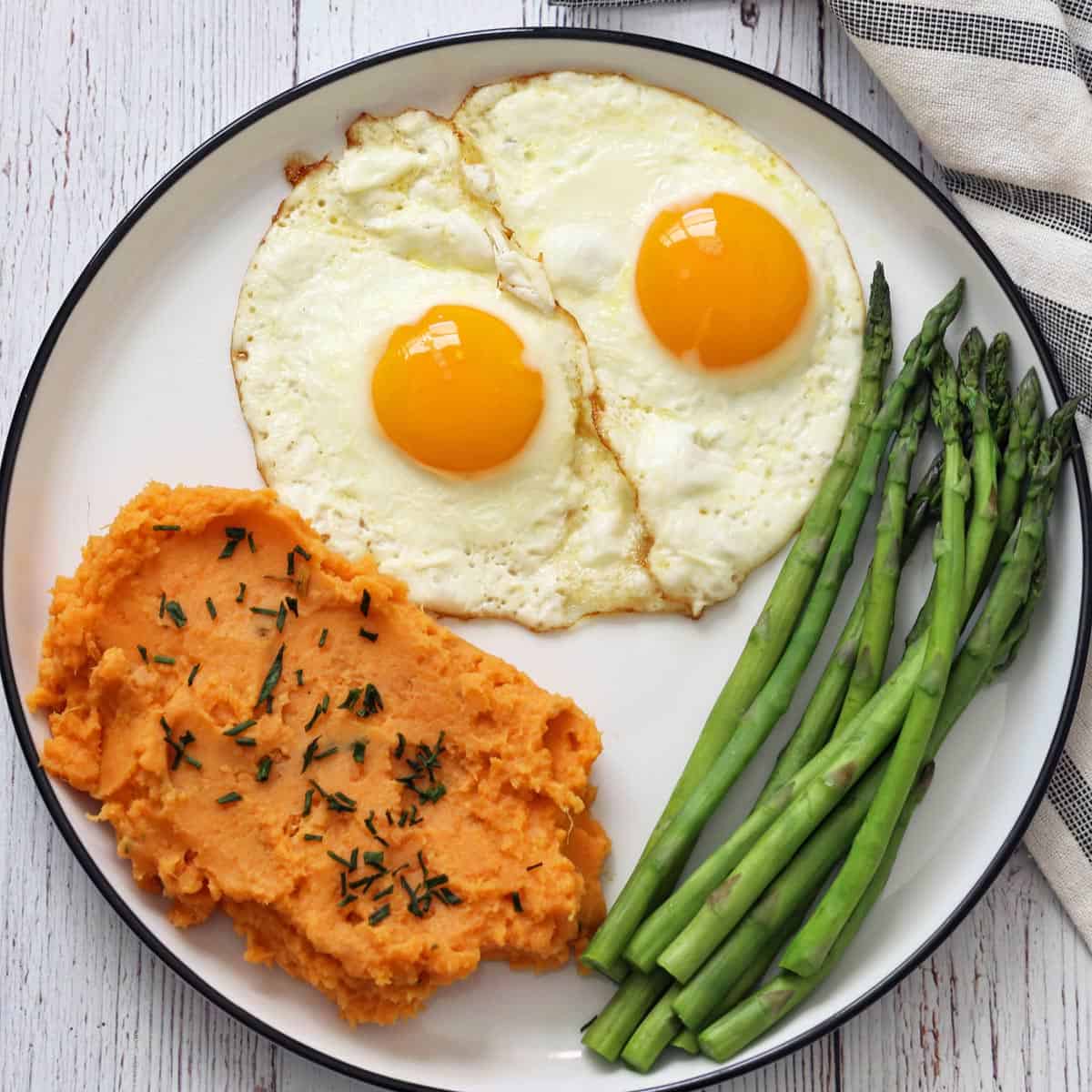Mashed sweet potatoes are served with eggs and asparagus.