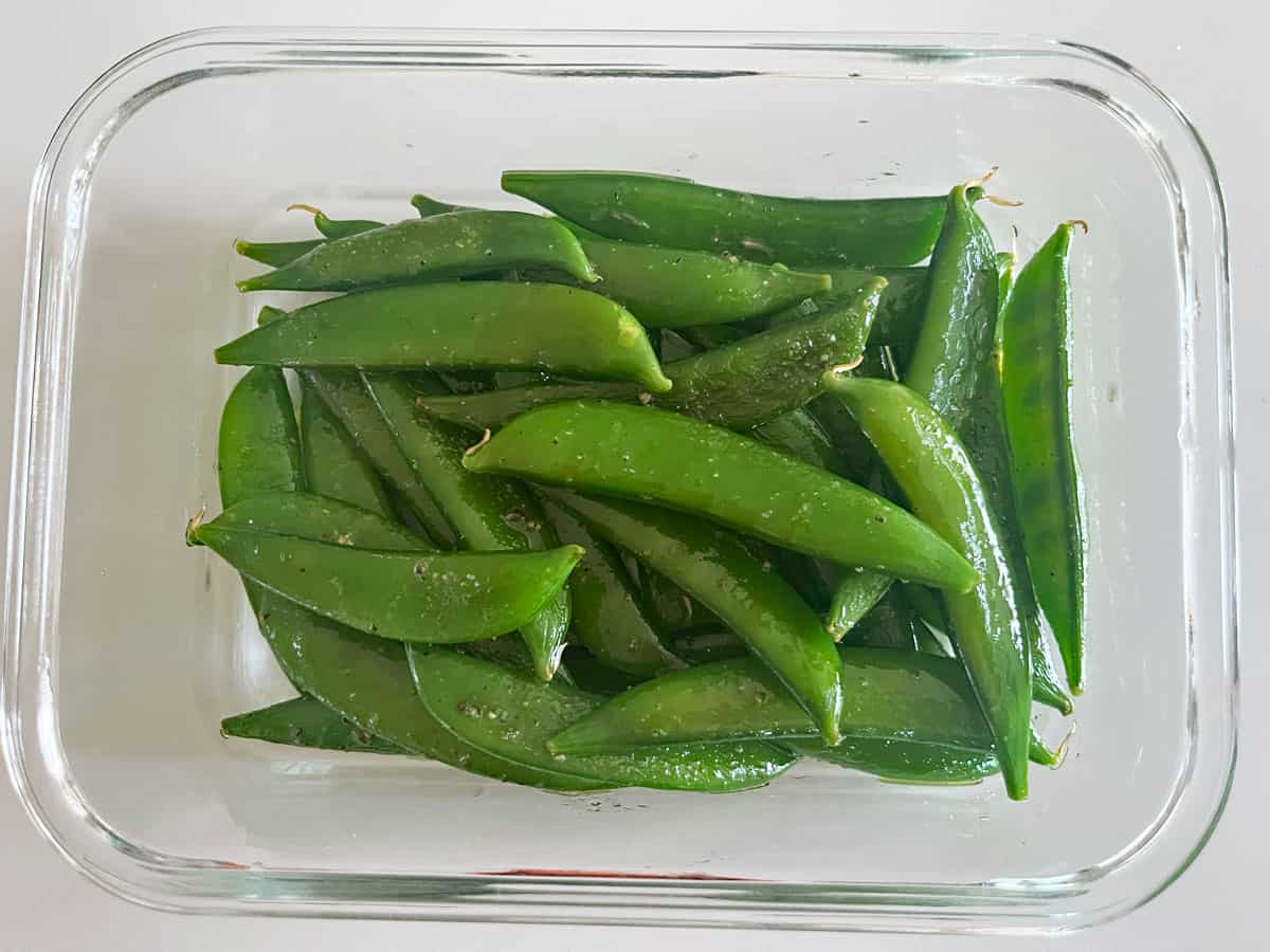 Leftover sugar snap peas are stored in a glass container.