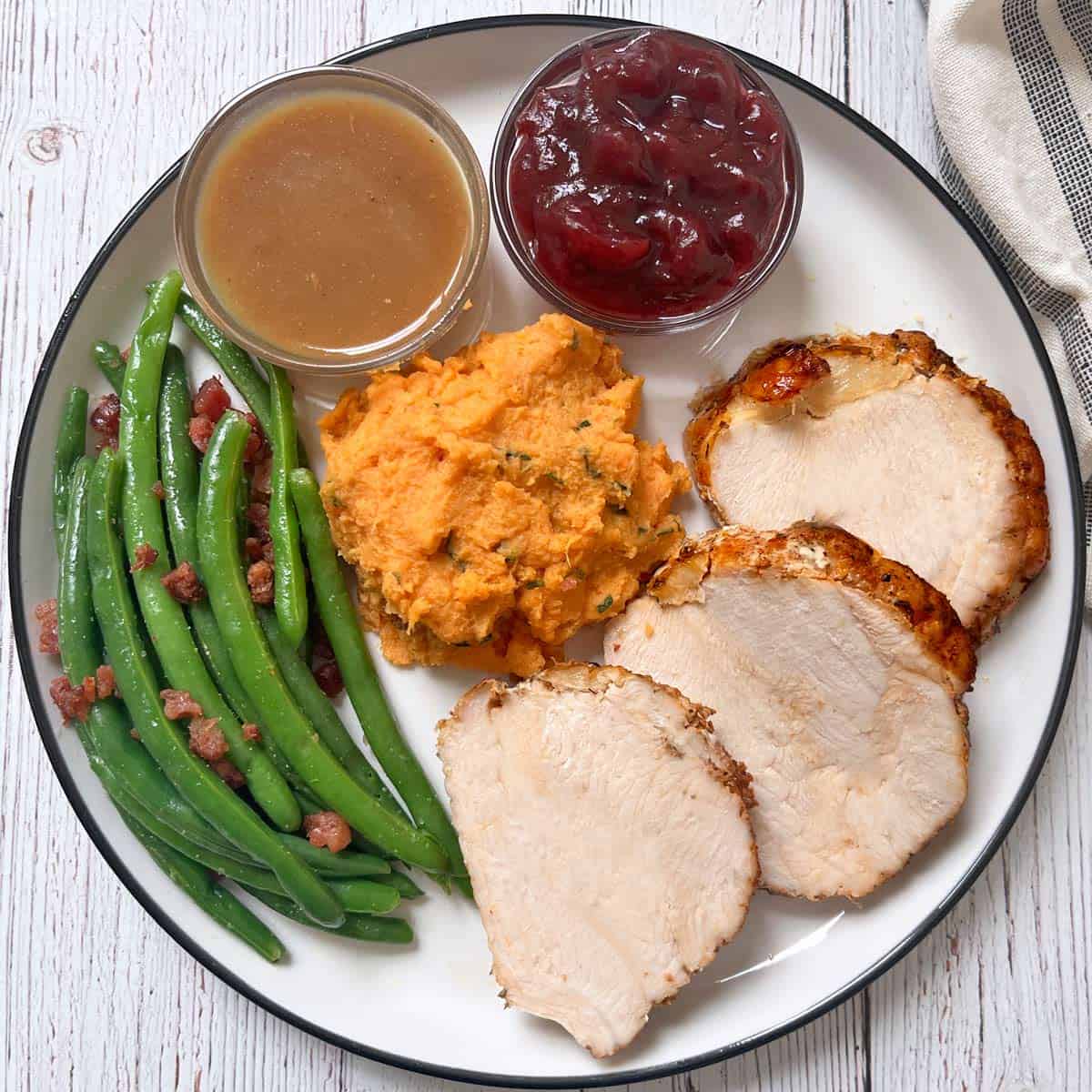 Roasted boneless turkey breast is serve with gravy, cranberry sauce, green beans, and mashed sweet potatoes.
