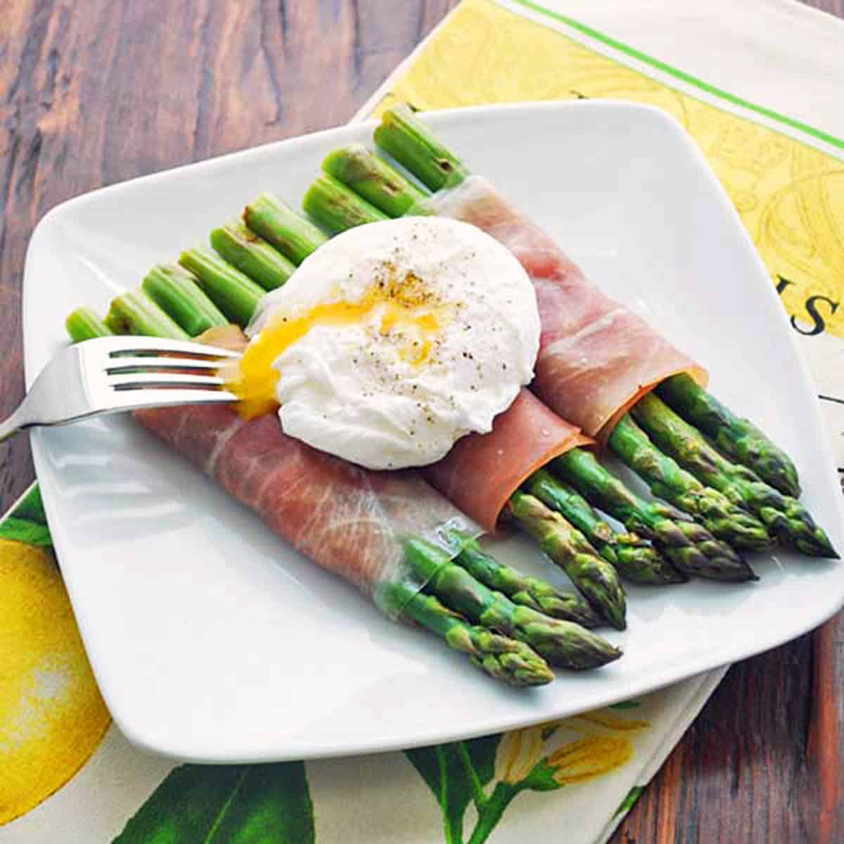 Prosciutto-wrapped asparagus bundles are topped with a poached egg.