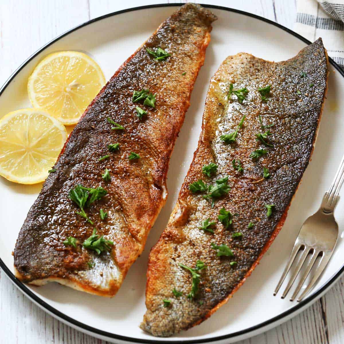 Two rainbow trout fillets are served on a plate with lemon slices.