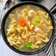Turkey soup is served in a dark soup bowl.