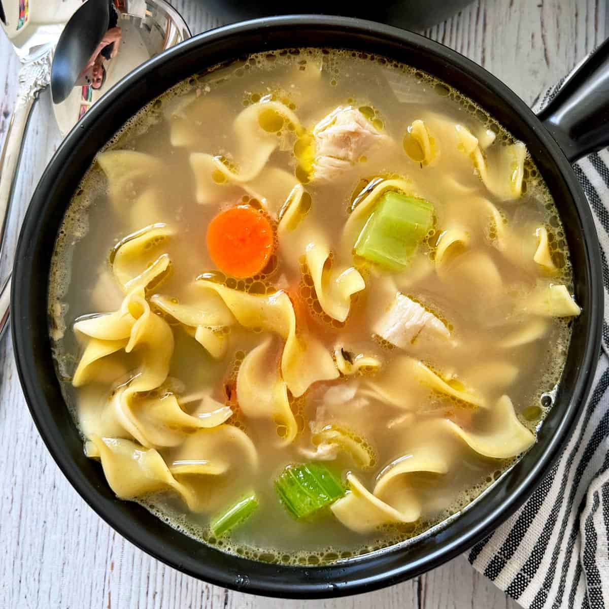 Turkey soup is served in a dark soup bowl.