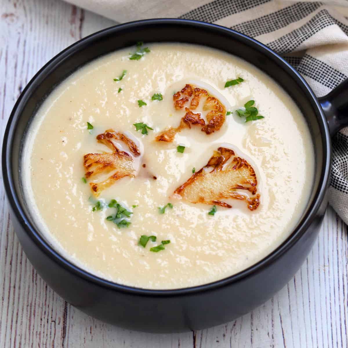 Cauliflower soup is served in a dark bowl.