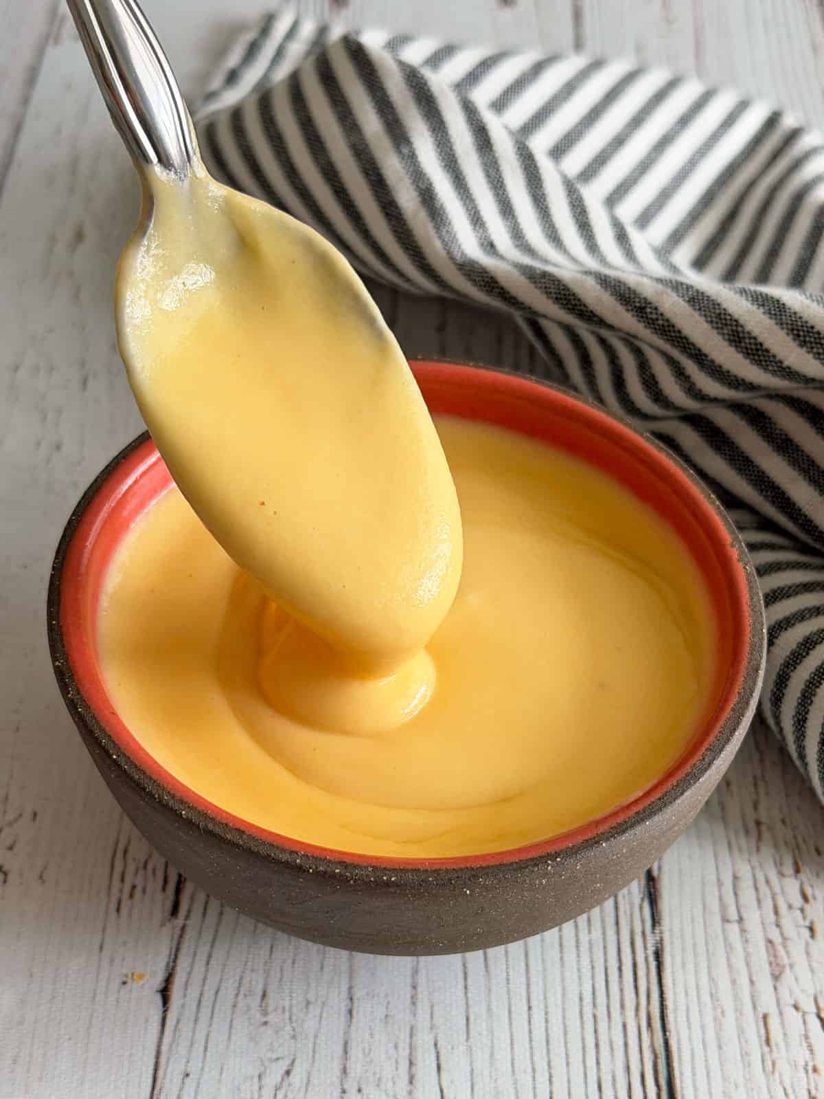 Cheese sauce is served in a bowl with a spoon.
