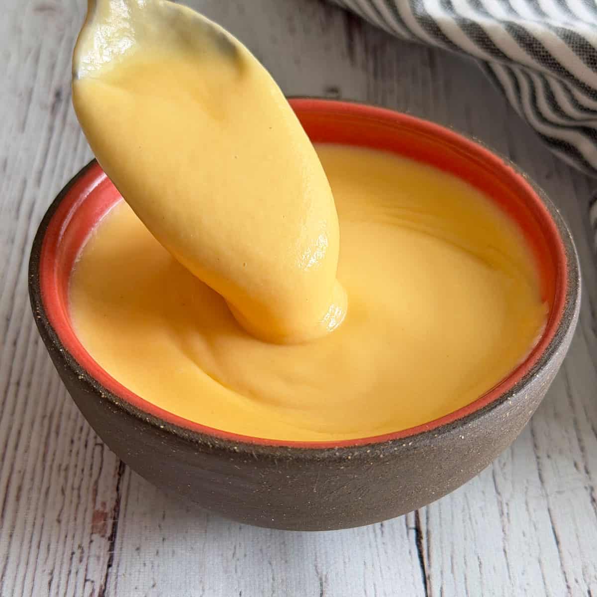 Cheese sauce is served in a bowl with a spoon.