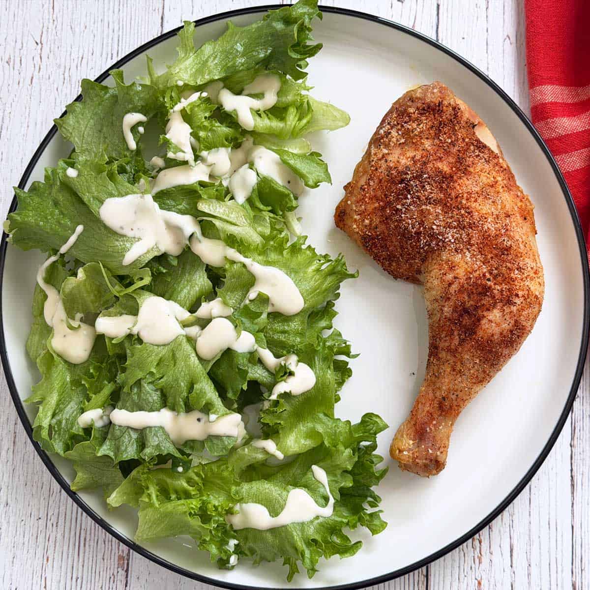 A chicken leg quarter is served with a salad.