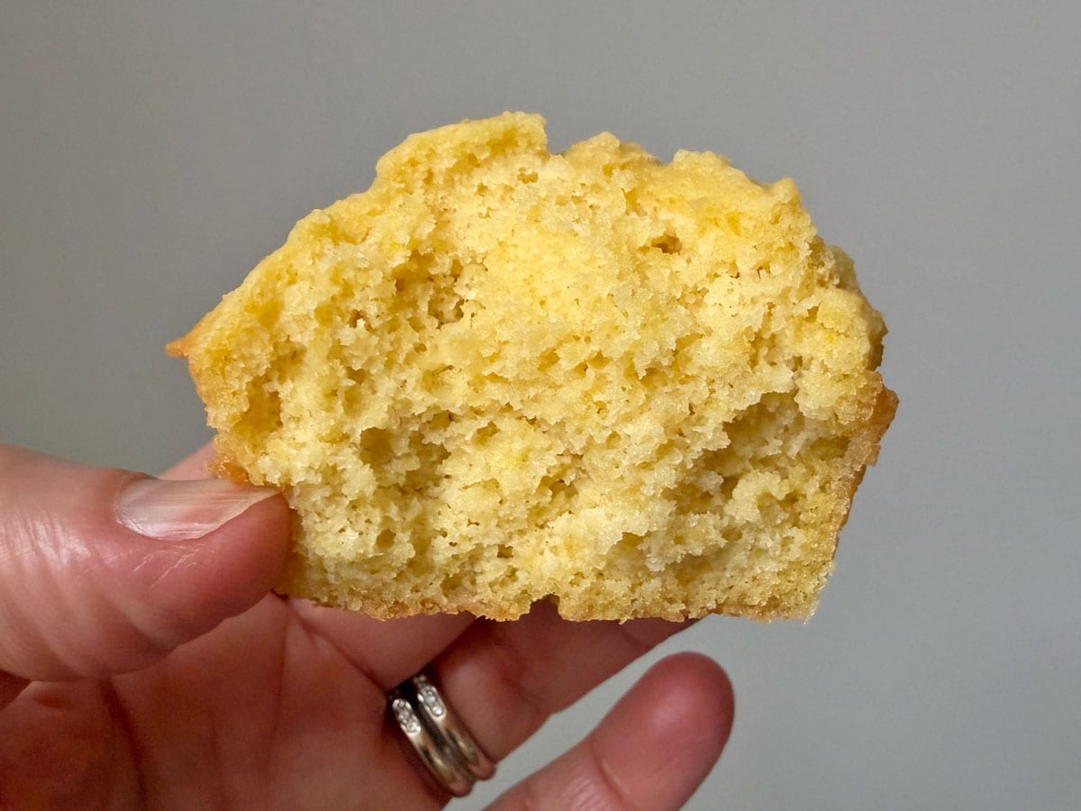 Holding a half-eaten cornbread muffin in the air to show its soft texture.