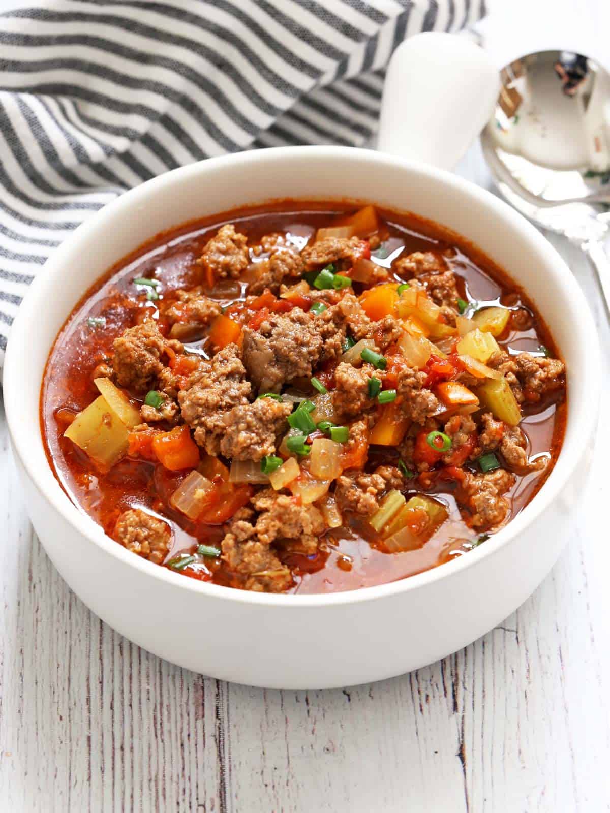 Hamburger soup is served in a white bowl with a spoon.