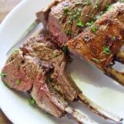 Rack of lamb is served on a white platter.