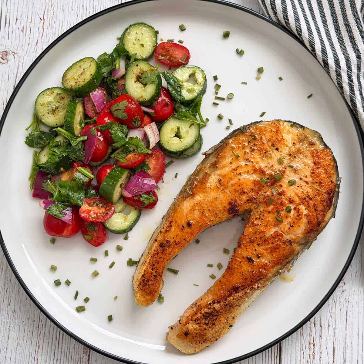 A salmon steak is served with a salad.