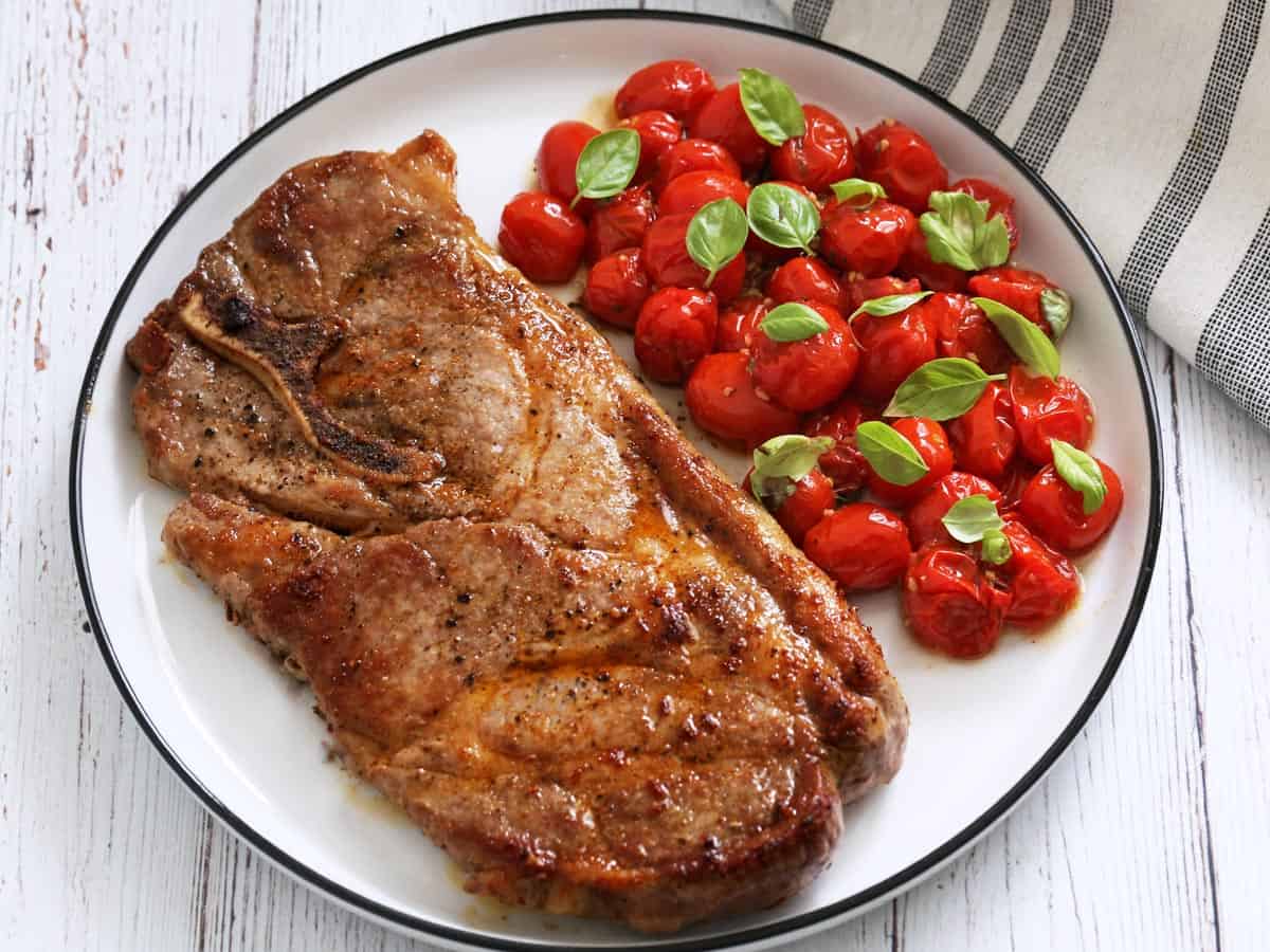 Roasted cherry tomatoes are served with pork steak.