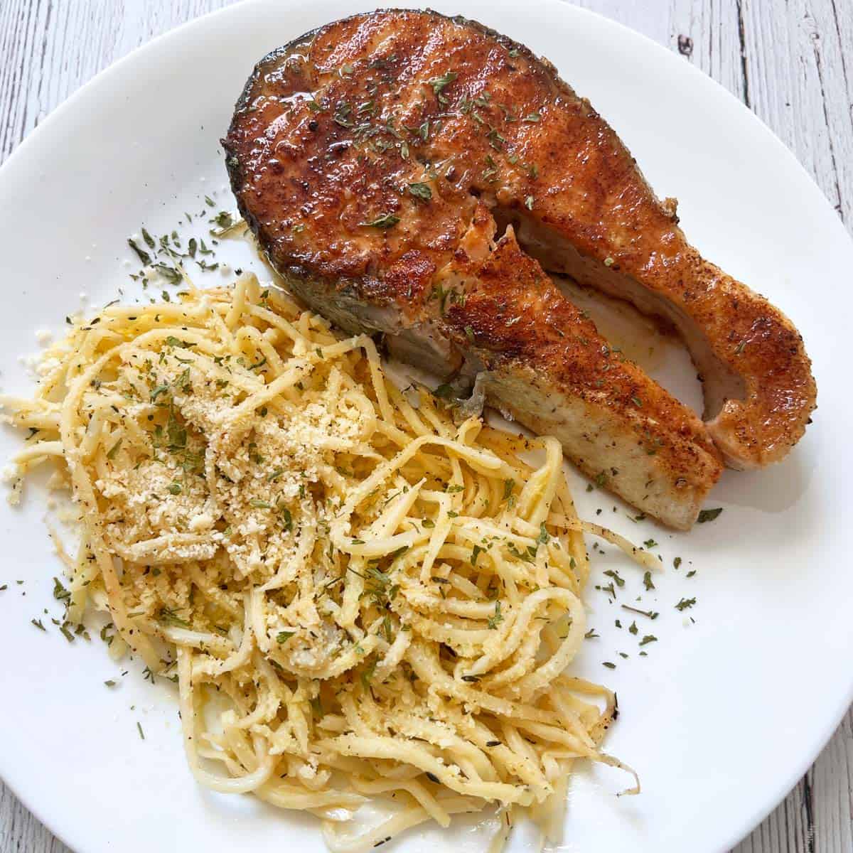 A salmon steak is served with pasta.